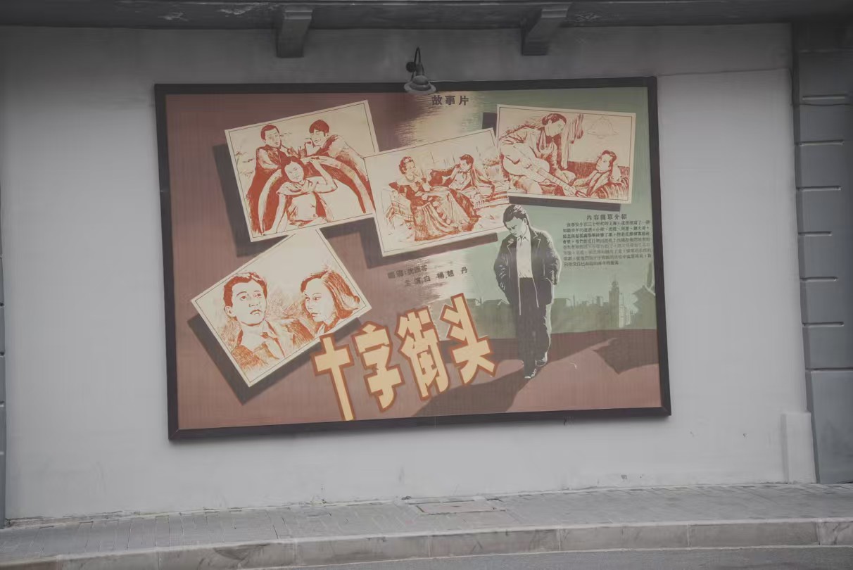 这是电影《十字街头》的复古海报，张贴于墙面。《十字街头》是经典老电影，海报用剧照拼接、艺术字体呈现片名，还有导演（沈西苓 ）、主演（赵丹等 ）等信息，以怀旧风格展现影片，唤起对老上海电影文化、经典作品的回忆，是复古场景营造、影视文化展示的元素，传递出浓厚的时代氛围与文艺气息 。